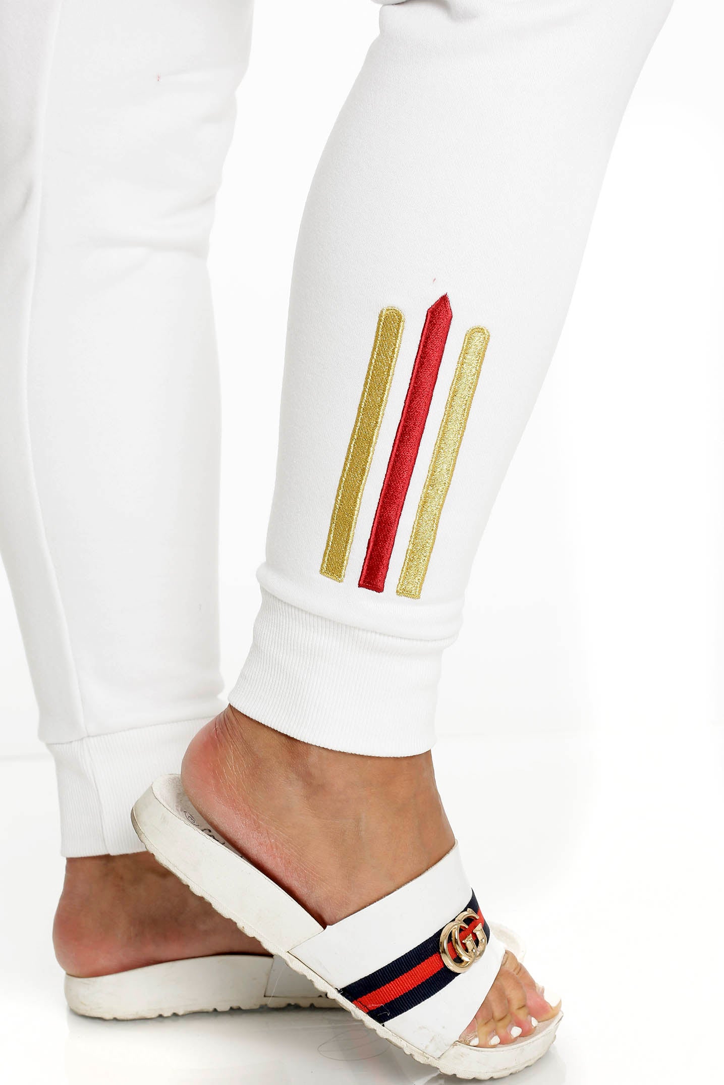 Bij de enkel van de witte broek zitten twee goudstrepen en één rode, boven een geribde boord.