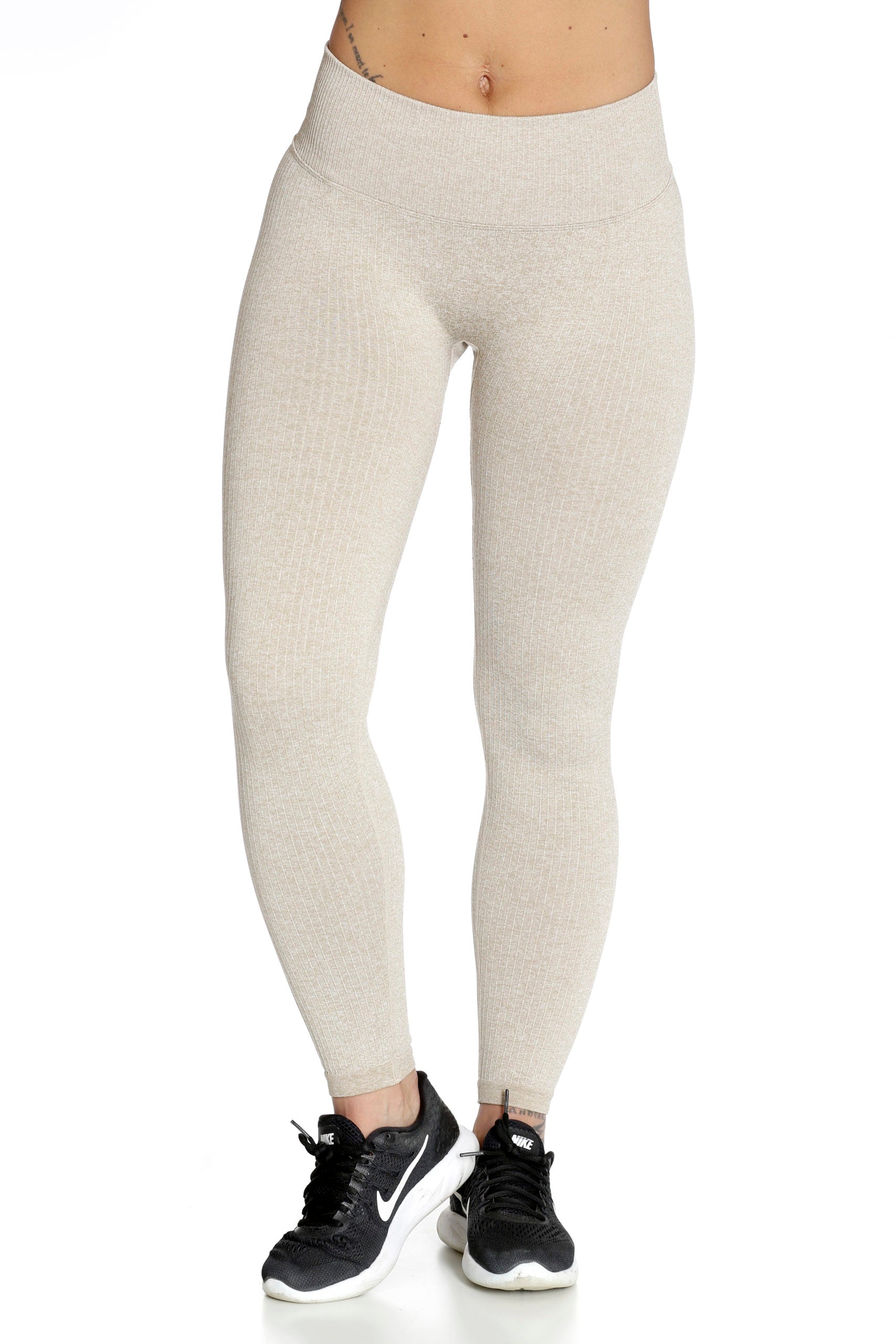 De brede tailleband zit hoog op de beige legging, de ribstructuur zichtbaar over het hele been.