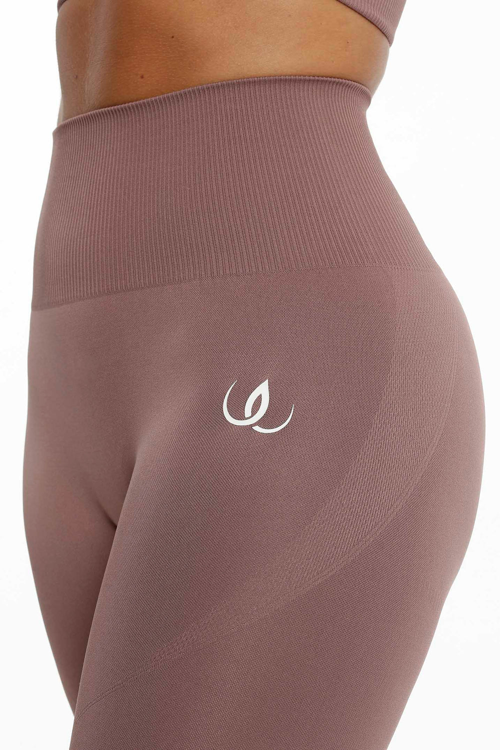 De geribbelde tailleband en het witte logo op de heup, de stof in een gedempte rosébruine tint.
