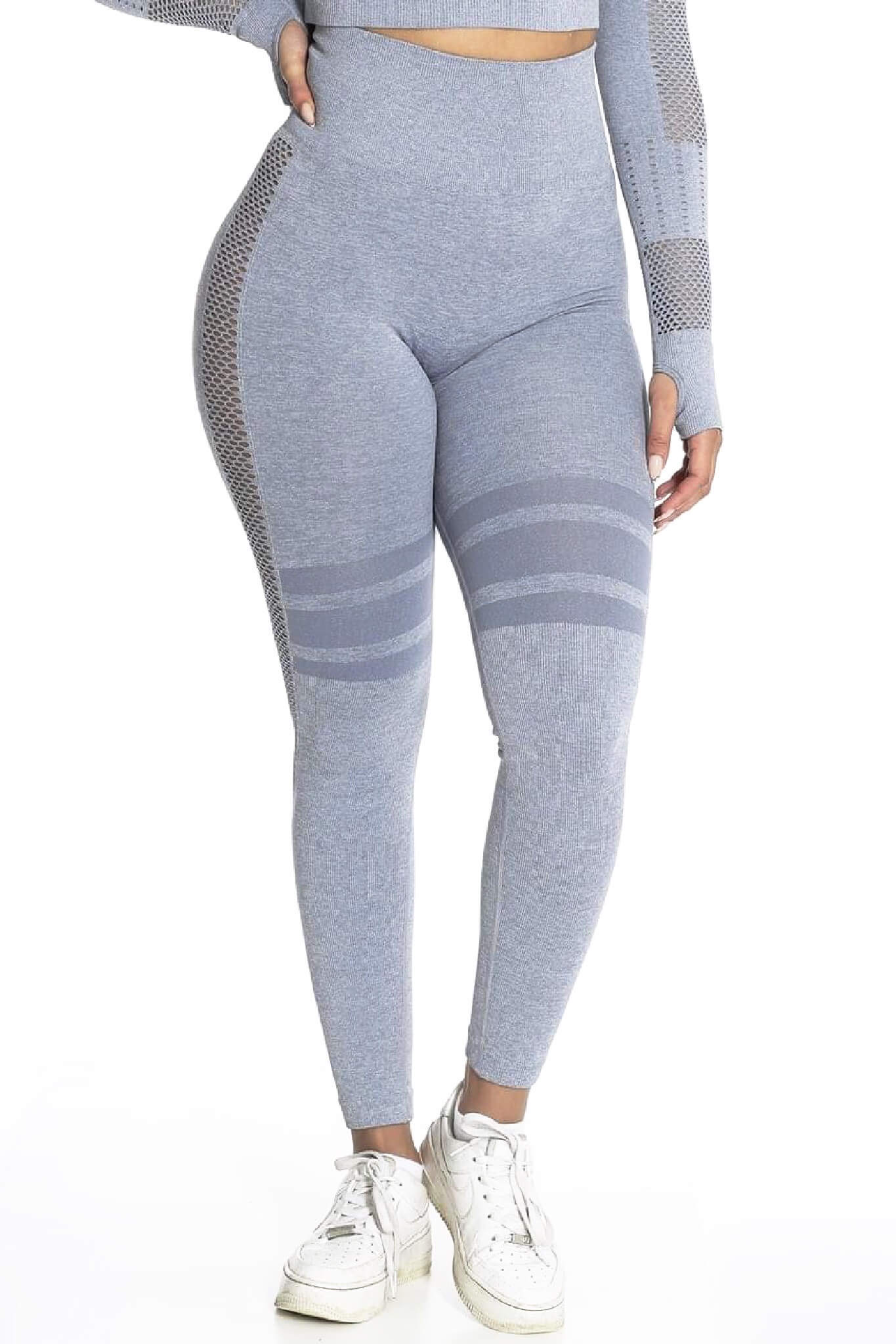De grijze legging zit hoog in de taille en heeft gestreepte banden over de dijen. Het model draagt witte sneakers.