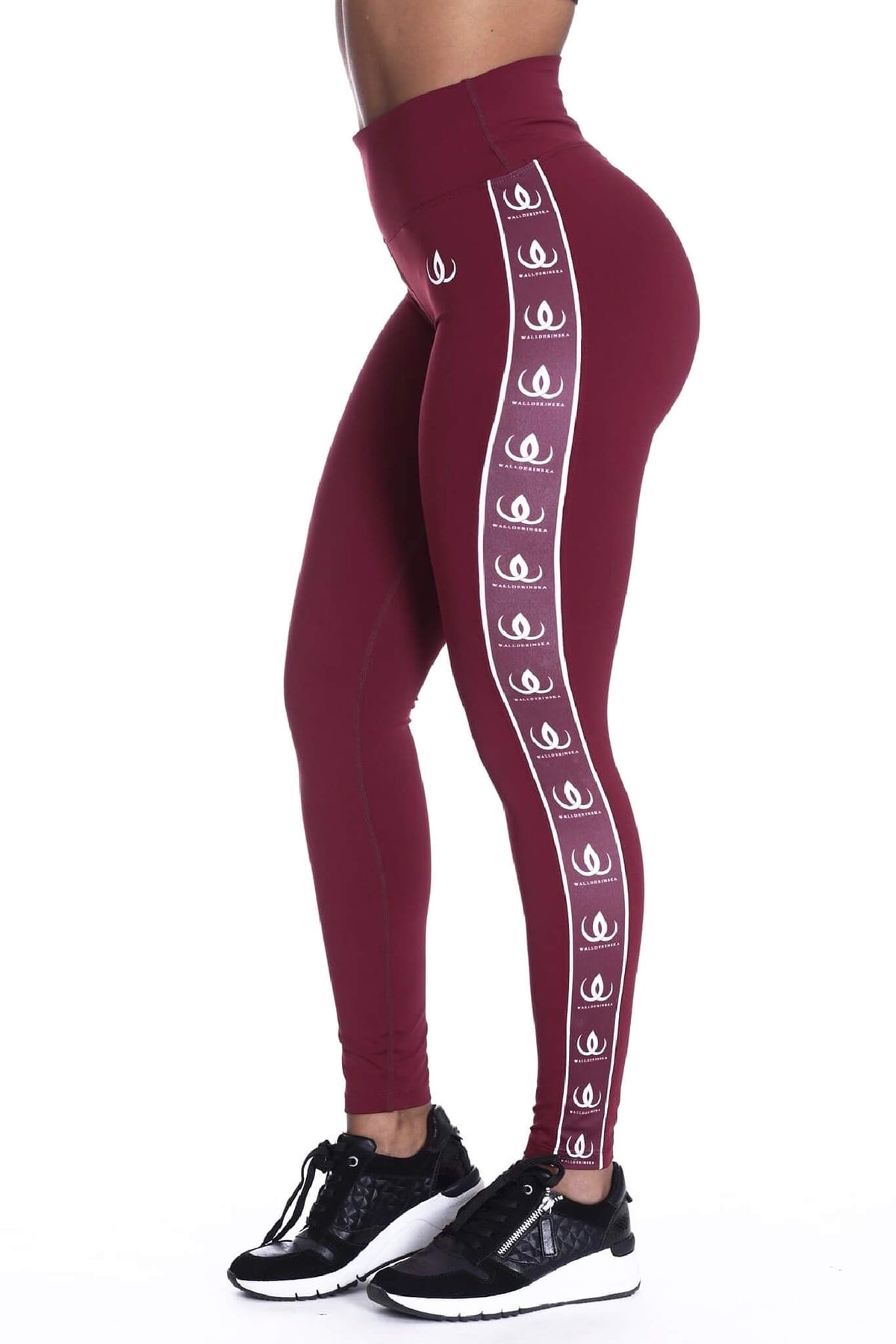 De hoge taille van de wijnrode legging, met witte logoband langs de zijkant en zwarte schoenen onderaan.