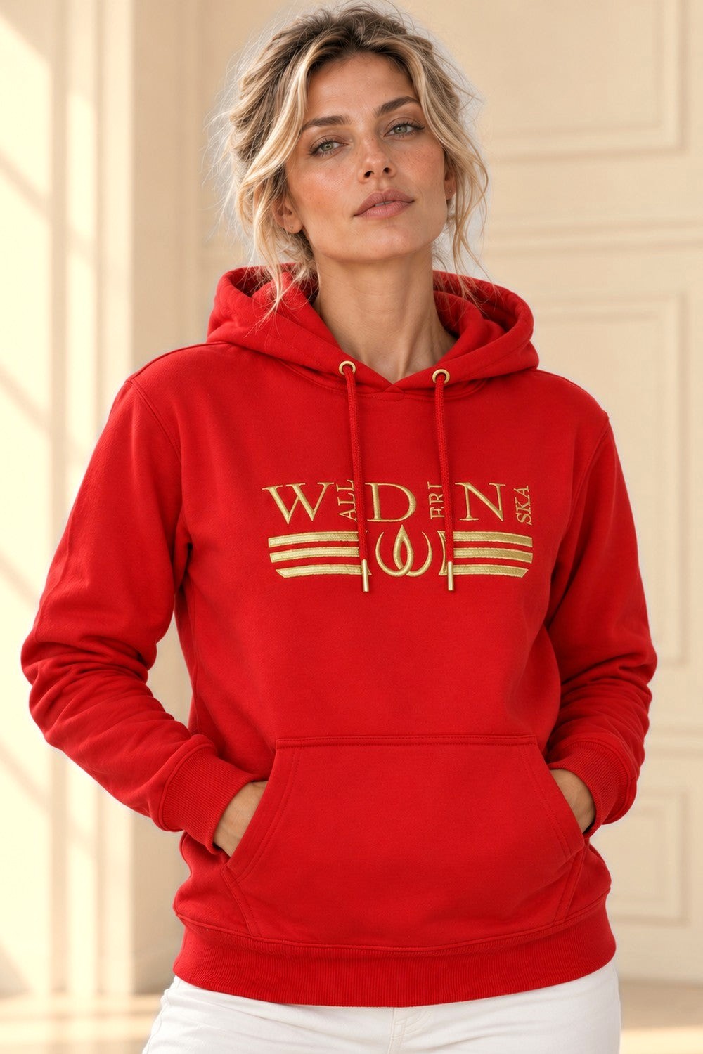 Rode Deluxe Hoodie met goudgeborduurd logo en gouden strepen over de borst, gedragen met een witte broek.