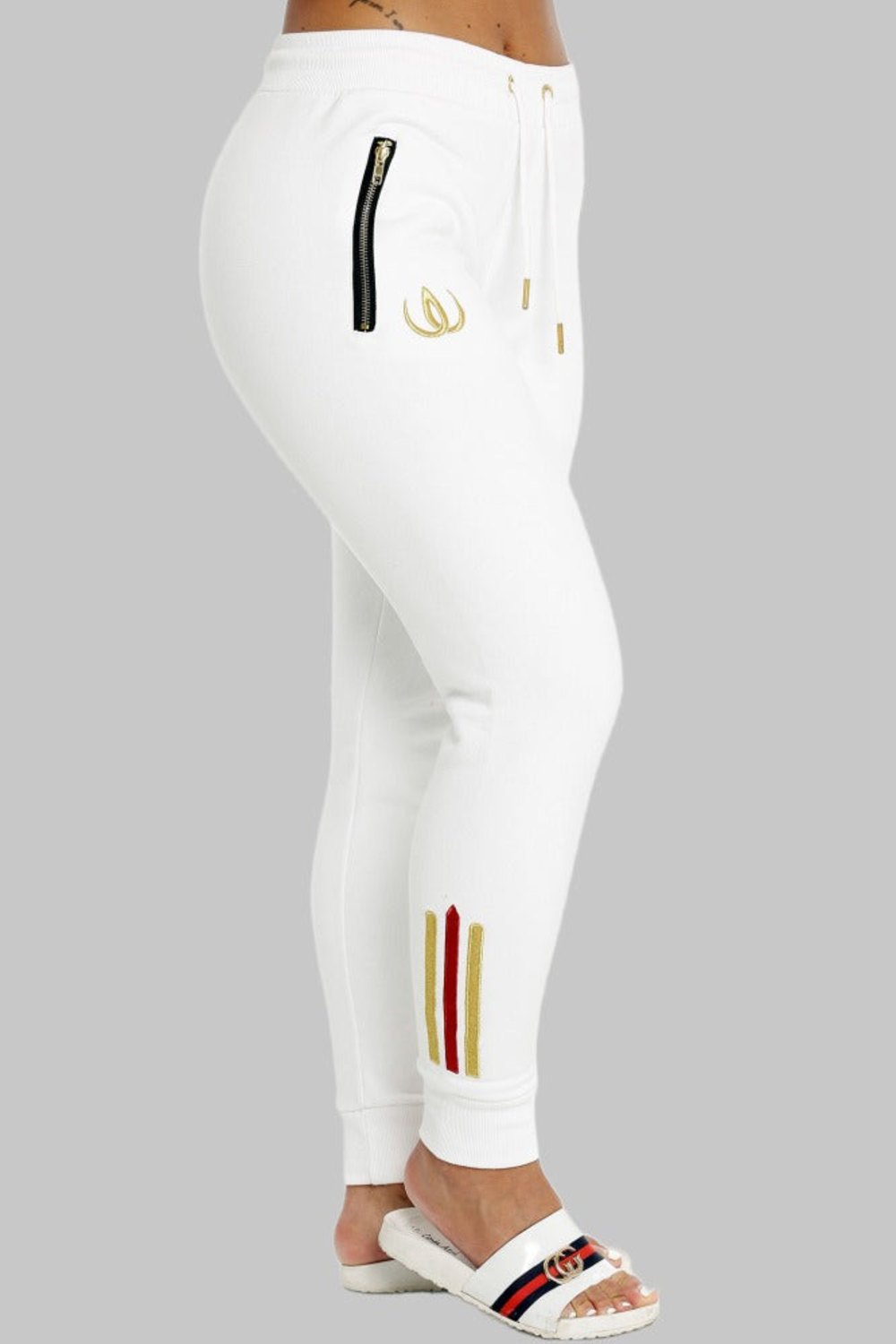 Witte joggers in profiel met goudkleurige rits in de zak, gouden logo op het dijbeen en strepen bij de enkel.