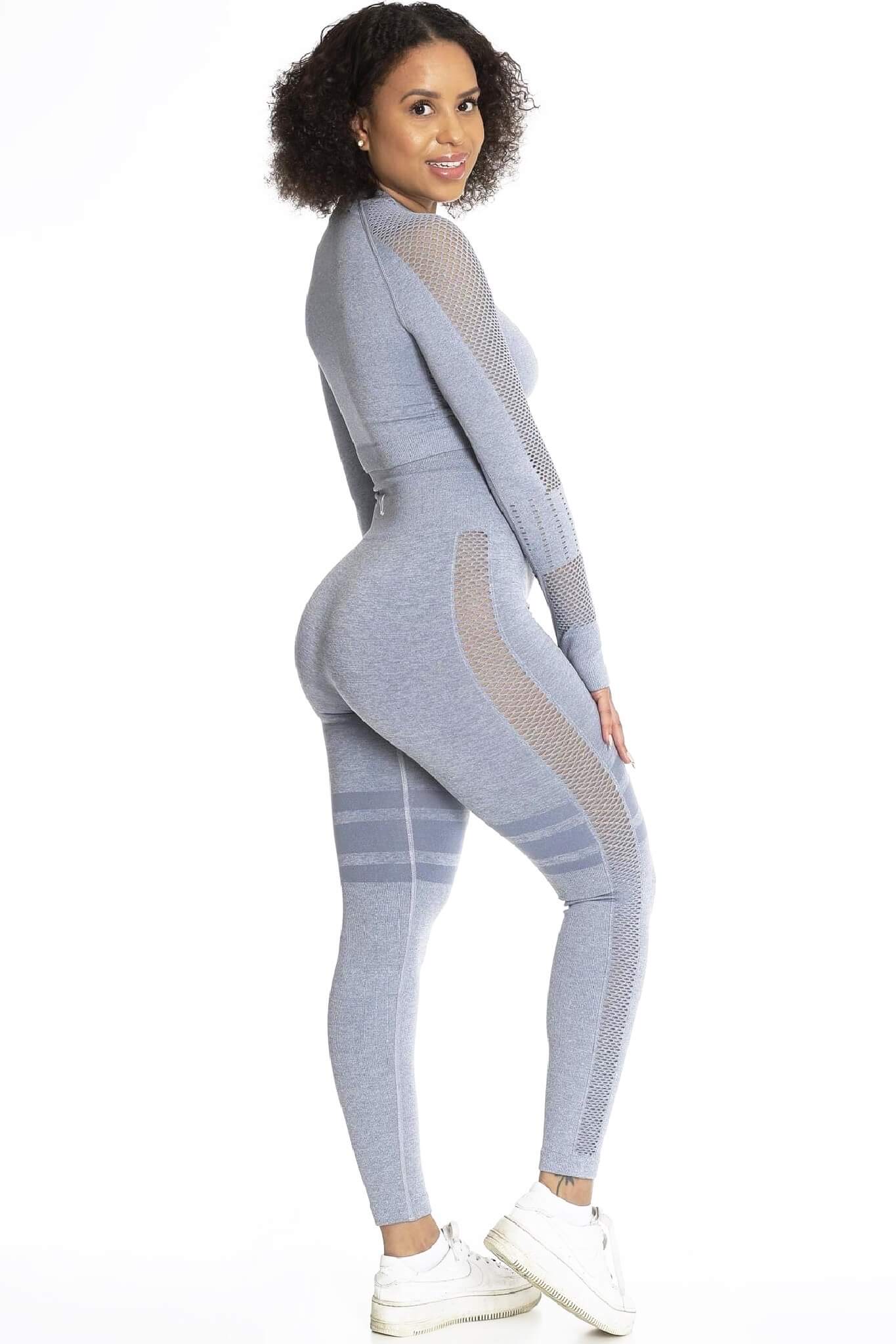 Het model kijkt over de schouder in een grijze legging en bijpassende trui, met witte sneakers.