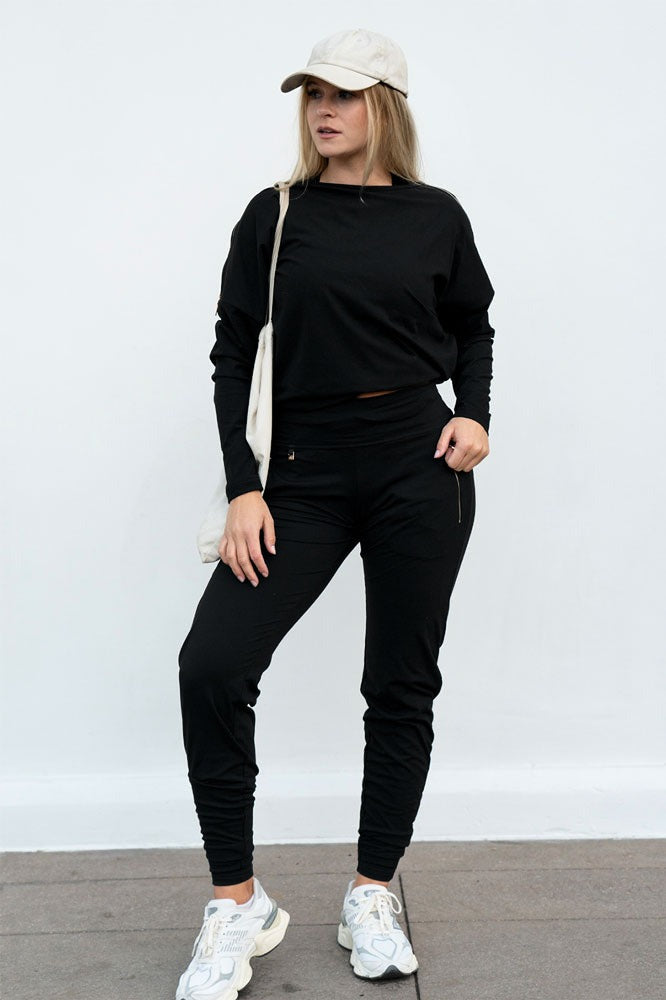 Een pet en canvas tas bij de broek en een korte zwarte sweater. Het model staat stil.