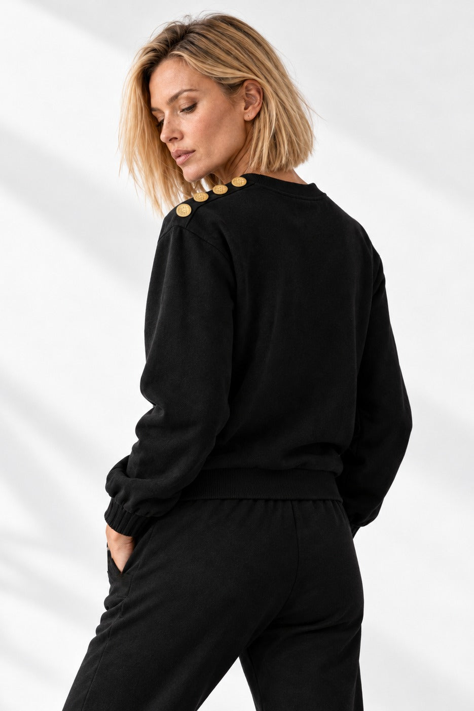 Edge Gold Button sweater schuin van achteren, met de gouden knopen langs de schouder.