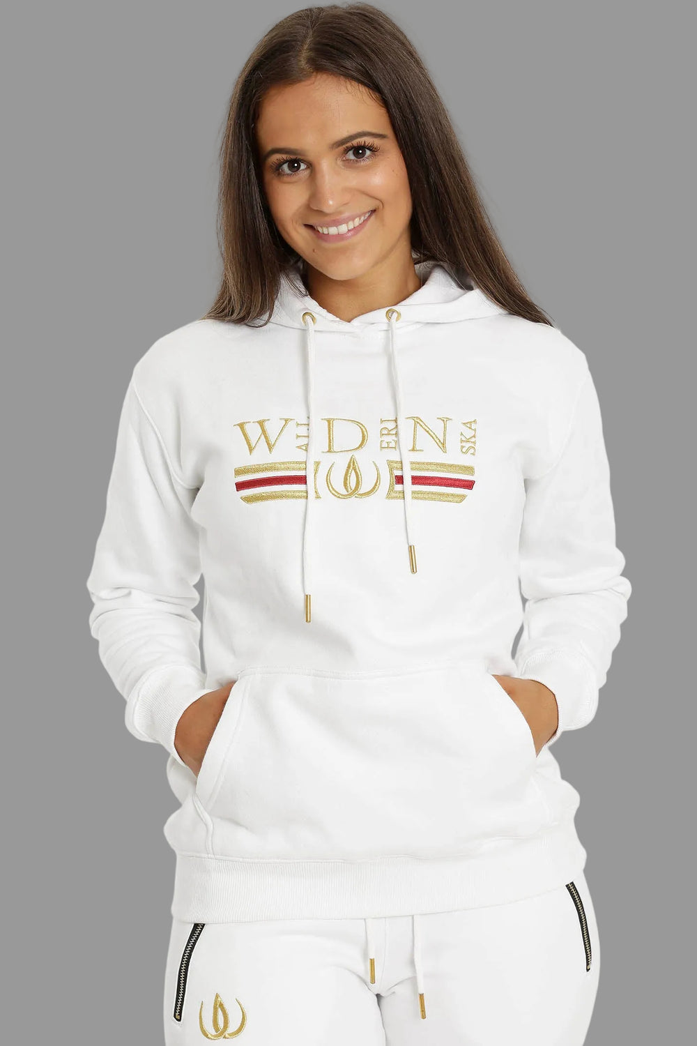 Witte hoodie met borduursel in goud en rood over de borst, gedragen met witte joggers met gouden logo.