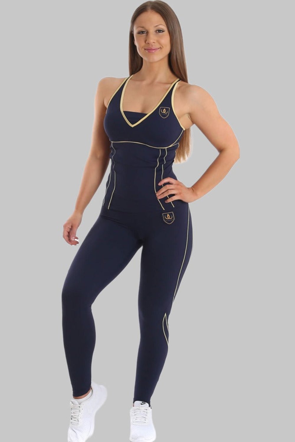 Het model staat in een marineblauwe top en marineblauwe legging met gouden lijnen, bij witte sneakers.