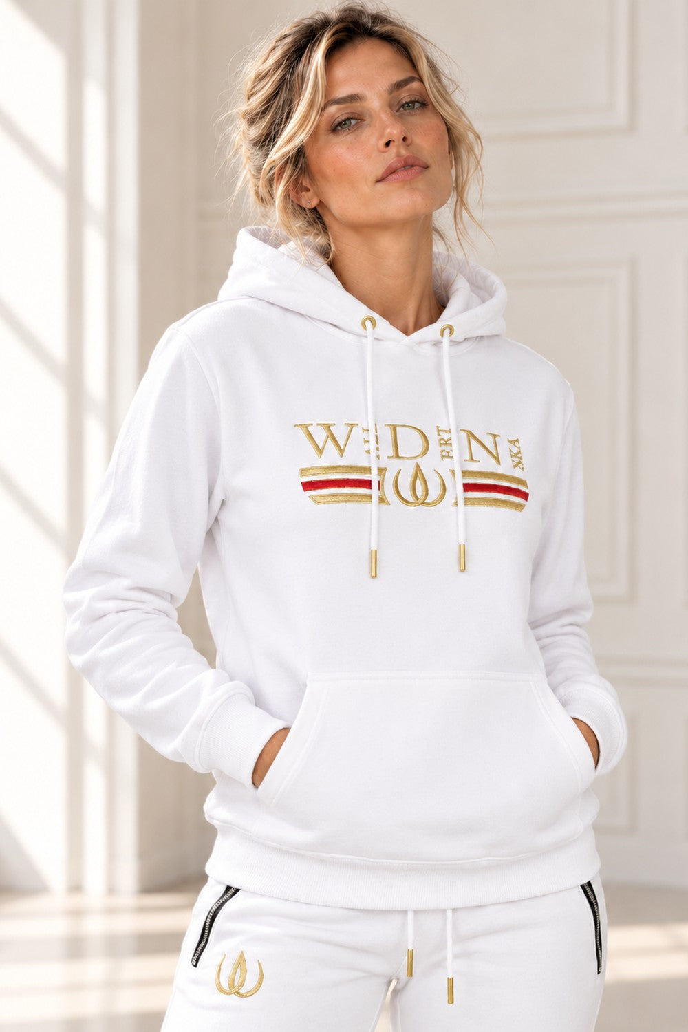Deluxe hoodie wit met goudgeborduurd logo, een rode en goudkleurige streep over de borst en koorden met gouden uiteinden.