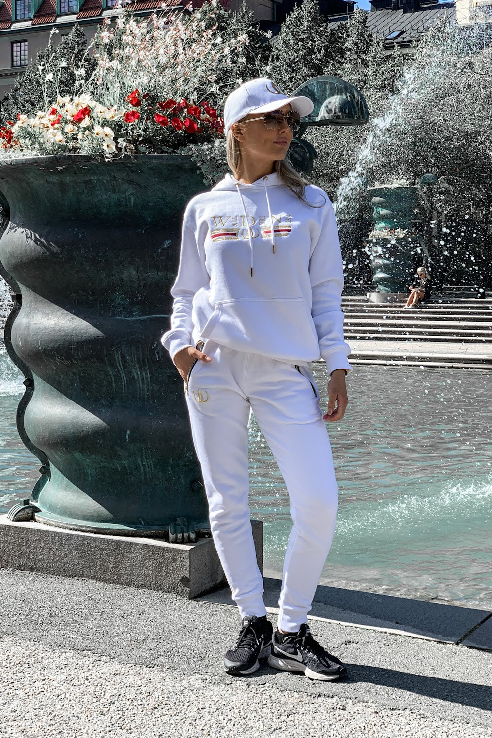 Bij een donkere urn staat het model met de handen in de zakken, in een witte hoodie en witte joggers.