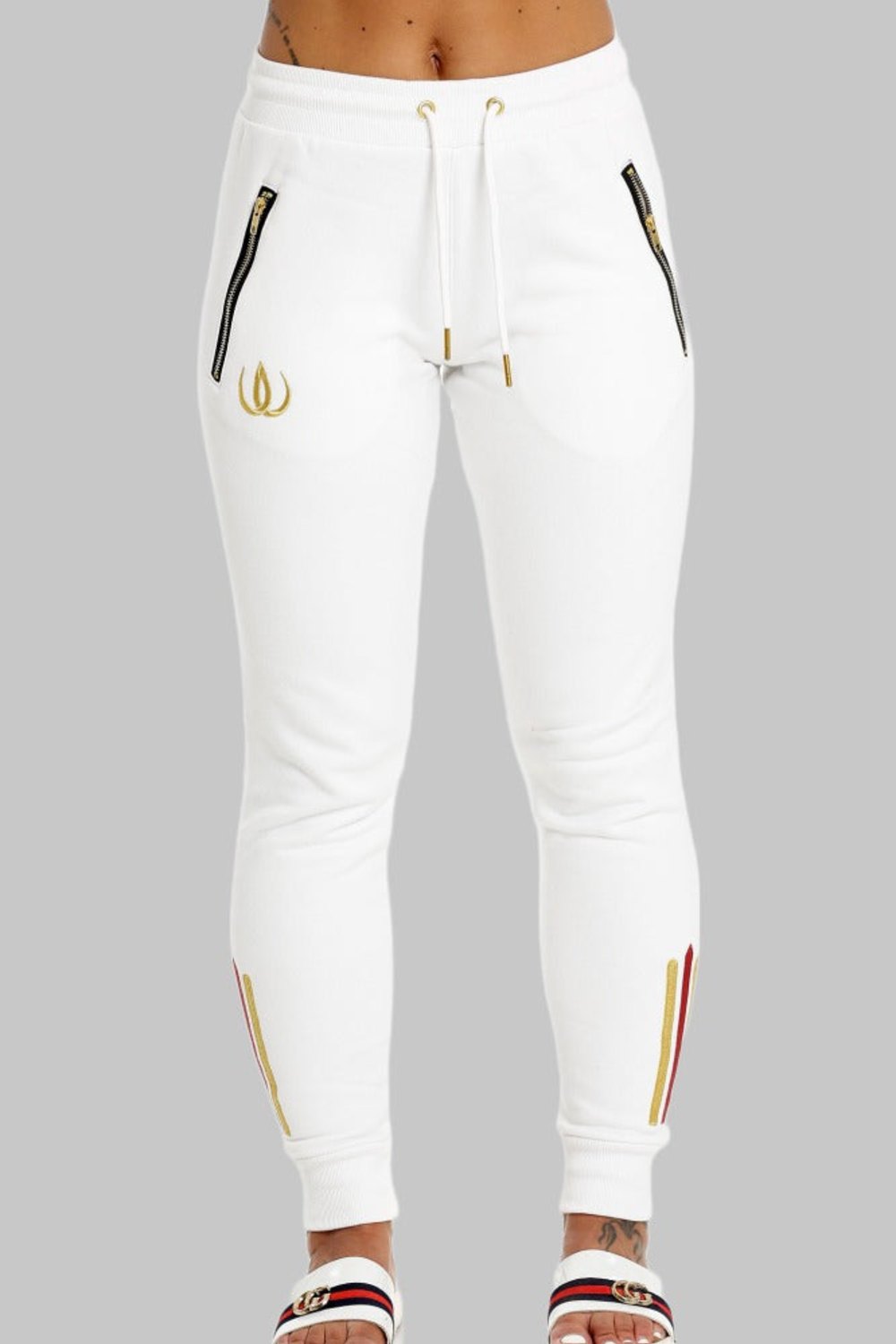 Twee goudkleurige ritszakken op de witte joggers, strikkoorden met gouden uiteinden en een gouden logo op het been.