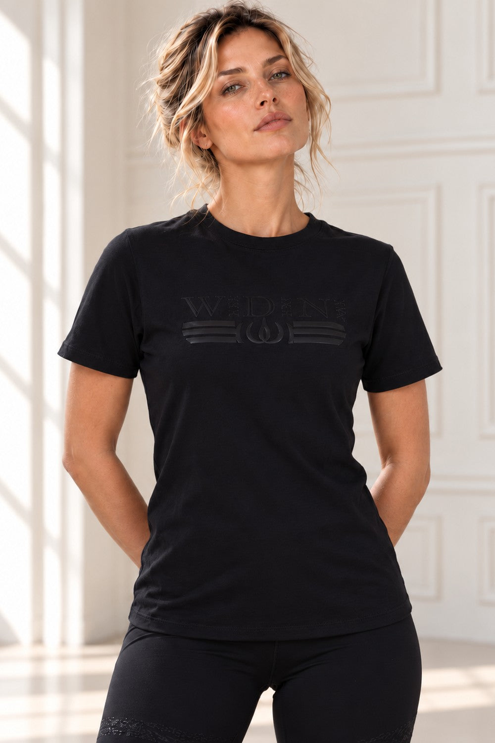 Zwarte Deluxe top met logo in dezelfde zwarte toon, gedragen met een zwarte legging.