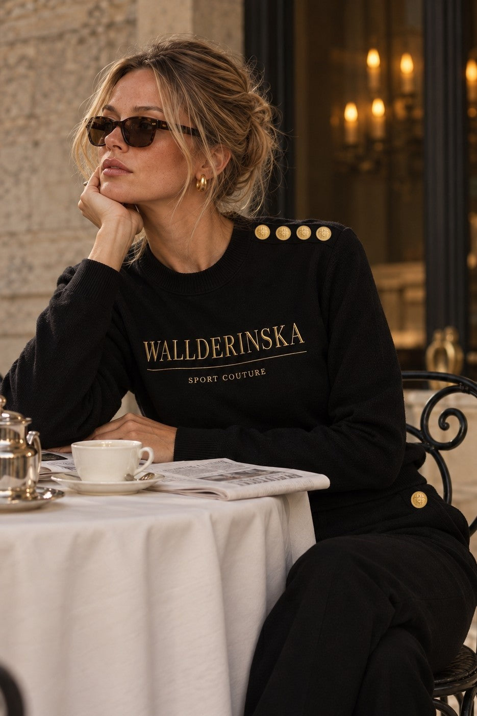 Edge Gold Button sweater in zwart in een café, met de gouden knopen op de schouder.