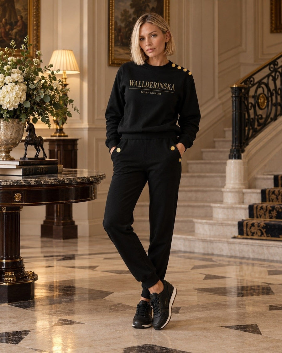 Edge Gold Button sweater en Edge Gold Button broek in een hal met een marmeren vloer.