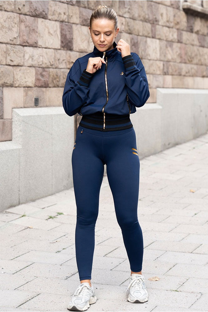 Het model draagt de marineblauwe legging en een jack in dezelfde toon met goudkleurige rits, in de stad.
